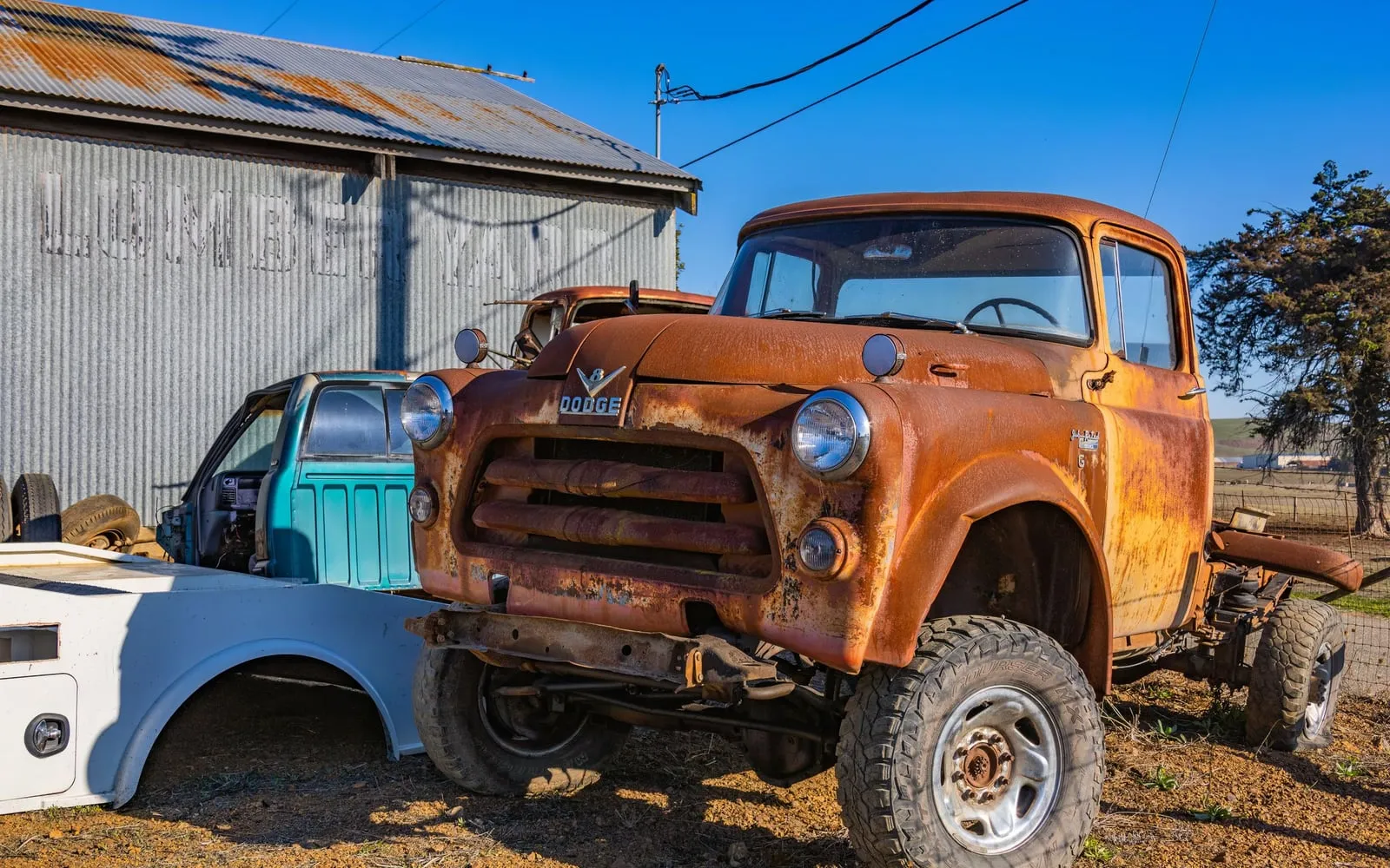 Rusted orange pickup truck parked in a gravel yard next to a metal shed